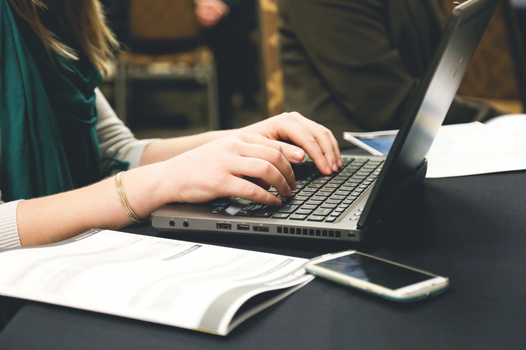 Person typing on laptop with smartphone nearby.